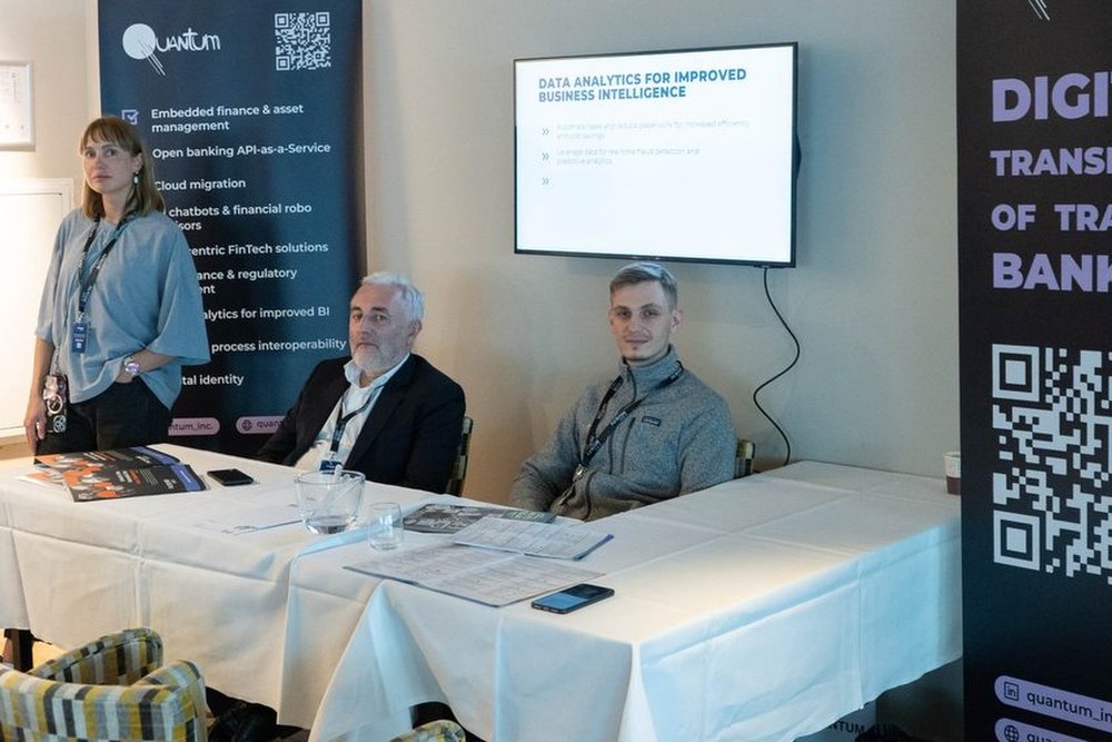 Two people seated at a table beside an exhibition stand at a previous Excellence in Digital Banking summit